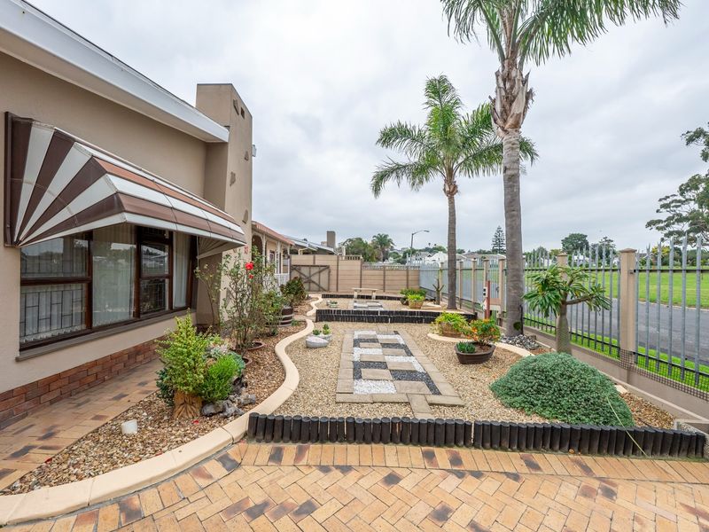 A well-maintained front garden area featuring brick paving, decorative gravel pathways, established palm trees, and secure metal perimeter fencing.