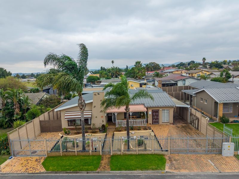 Aerial view of a single-story residential property featuring a metal roof, paved driveway, secure perimeter fencing, and a covered front patio area.
