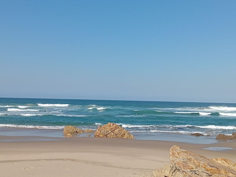 A scenic view of the ocean coastline featuring sandy beach and natural rock formations.