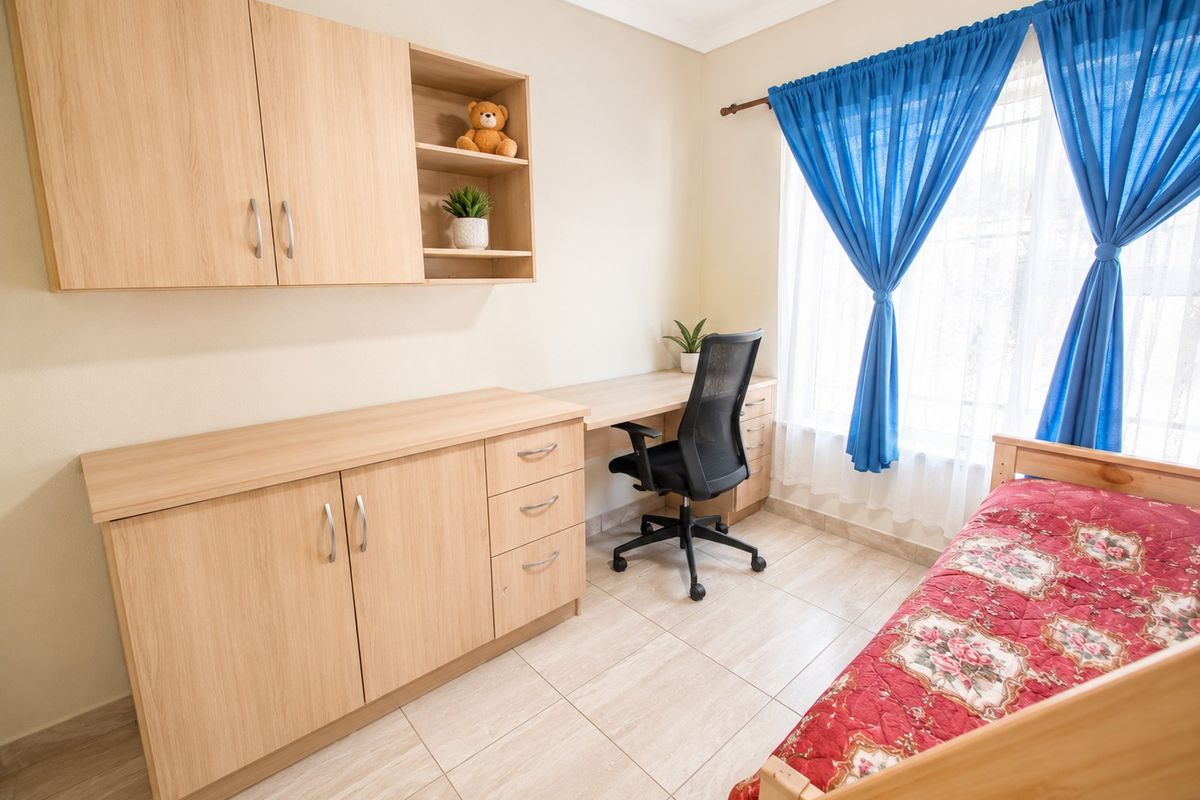 A well-maintained bedroom featuring light wood built-in cabinetry and a matching integrated desk, complemented by neutral tiled flooring.