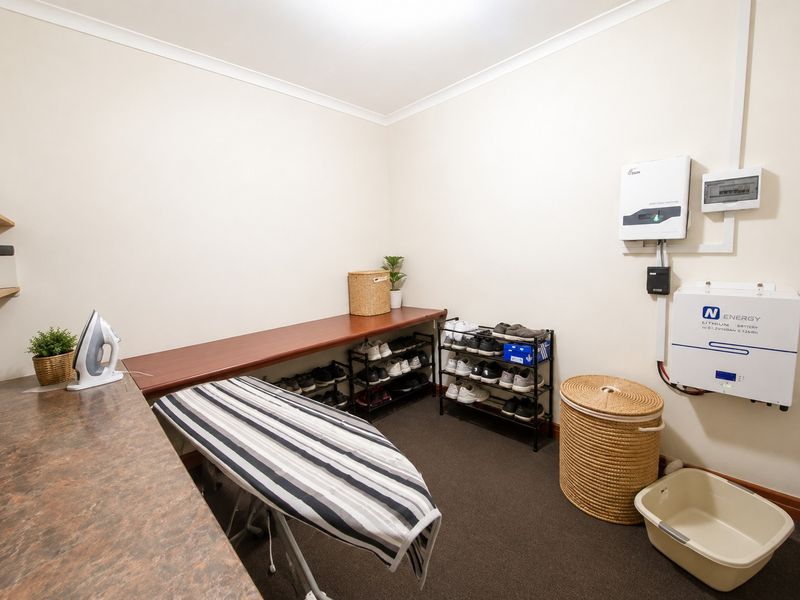 A functional utility room featuring built-in shelving, laminate work surfaces, and a wall-mounted solar power inverter and lithium battery system.
