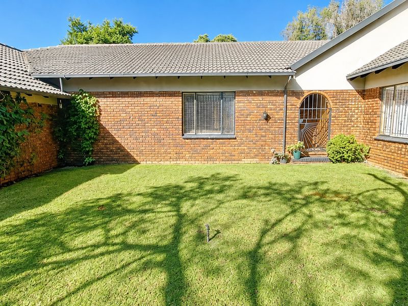 A rear view of the property featuring a brick facade, tiled roof, and a well-maintained lawn area with security features on windows and doors.