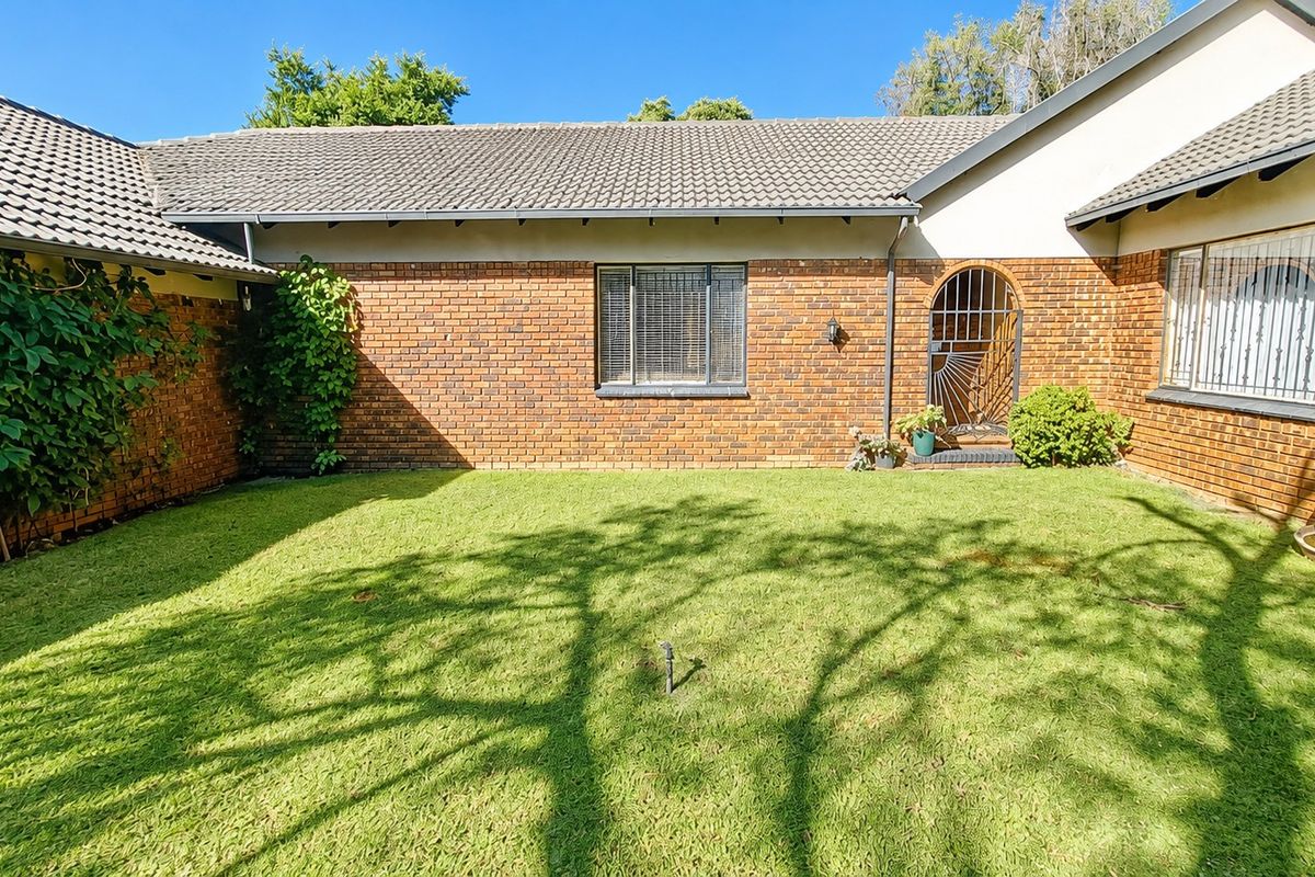 A rear view of the property featuring a brick facade, tiled roof, and a well-maintained lawn area with security features on windows and doors.