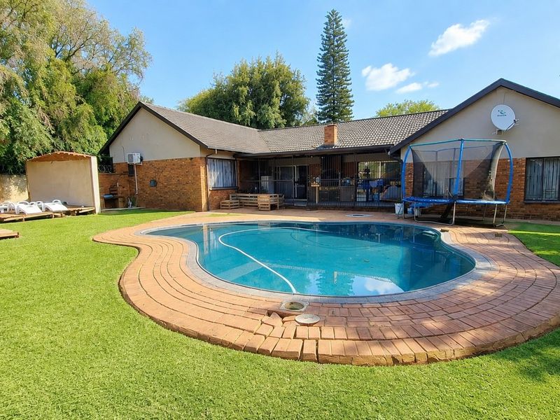 Rear view of the property featuring a swimming pool with brick paving, timber decking, and a spacious garden area.