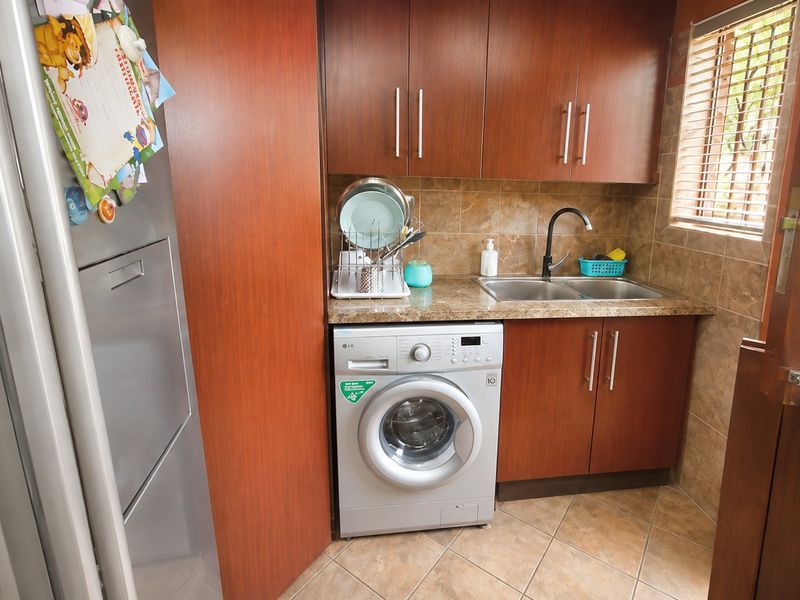 Compact laundry area featuring built-in wooden cabinetry, granite countertops, a double stainless steel sink, and tiled finishes.
