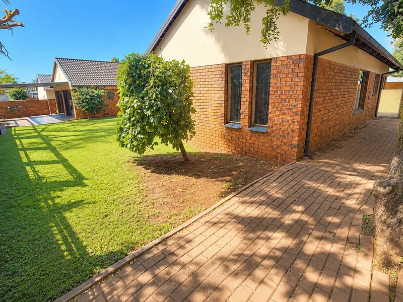 A view of the rear exterior featuring a brick facade, paved walkway, and a well-maintained lawn area.