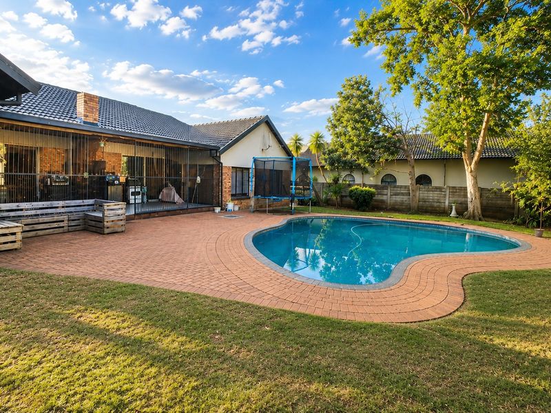 Spacious backyard featuring a kidney-shaped swimming pool, extensive brick-paved patio area, security fencing, and a well-maintained garden with mature trees.