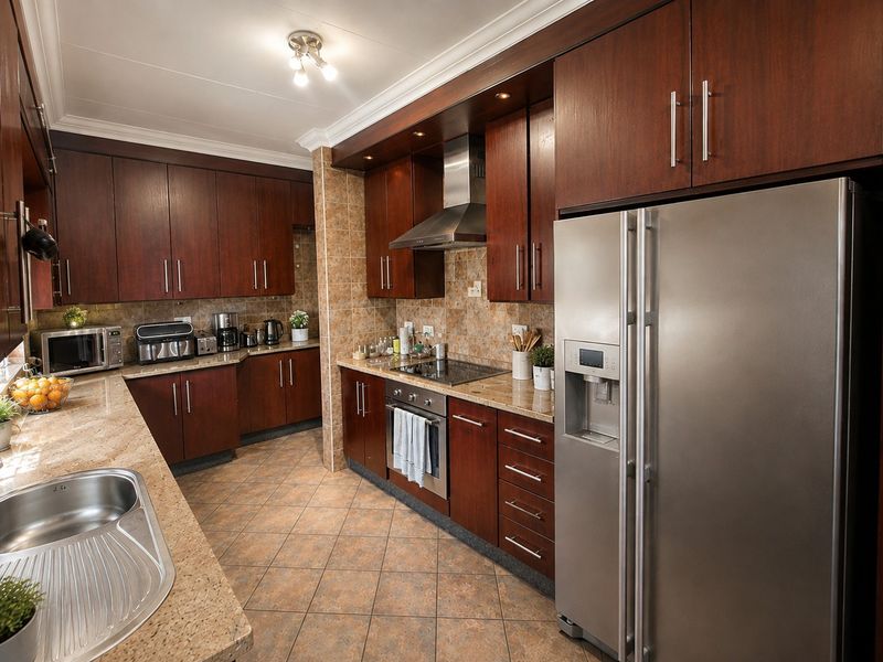 A well-appointed kitchen featuring dark wood cabinetry, granite countertops, integrated stainless steel appliances, and tiled finishes throughout.