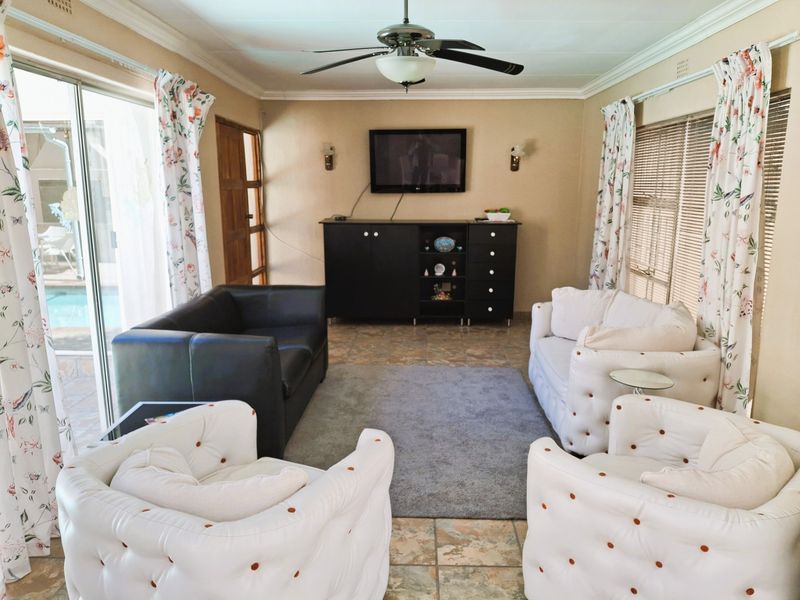 A comfortable living room featuring tiled flooring, a ceiling fan, and large sliding glass doors providing natural light and access to the outdoor pool area.