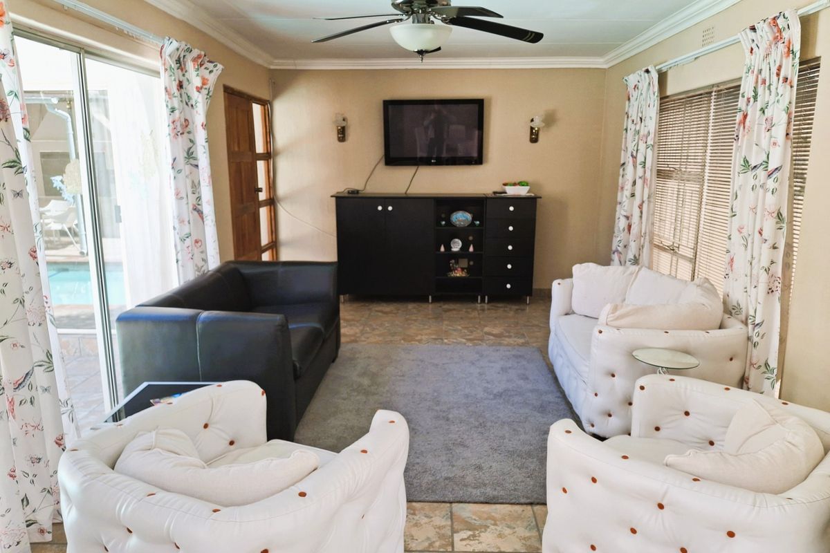A comfortable living room featuring tiled flooring, a ceiling fan, and large sliding glass doors providing natural light and access to the outdoor pool area.