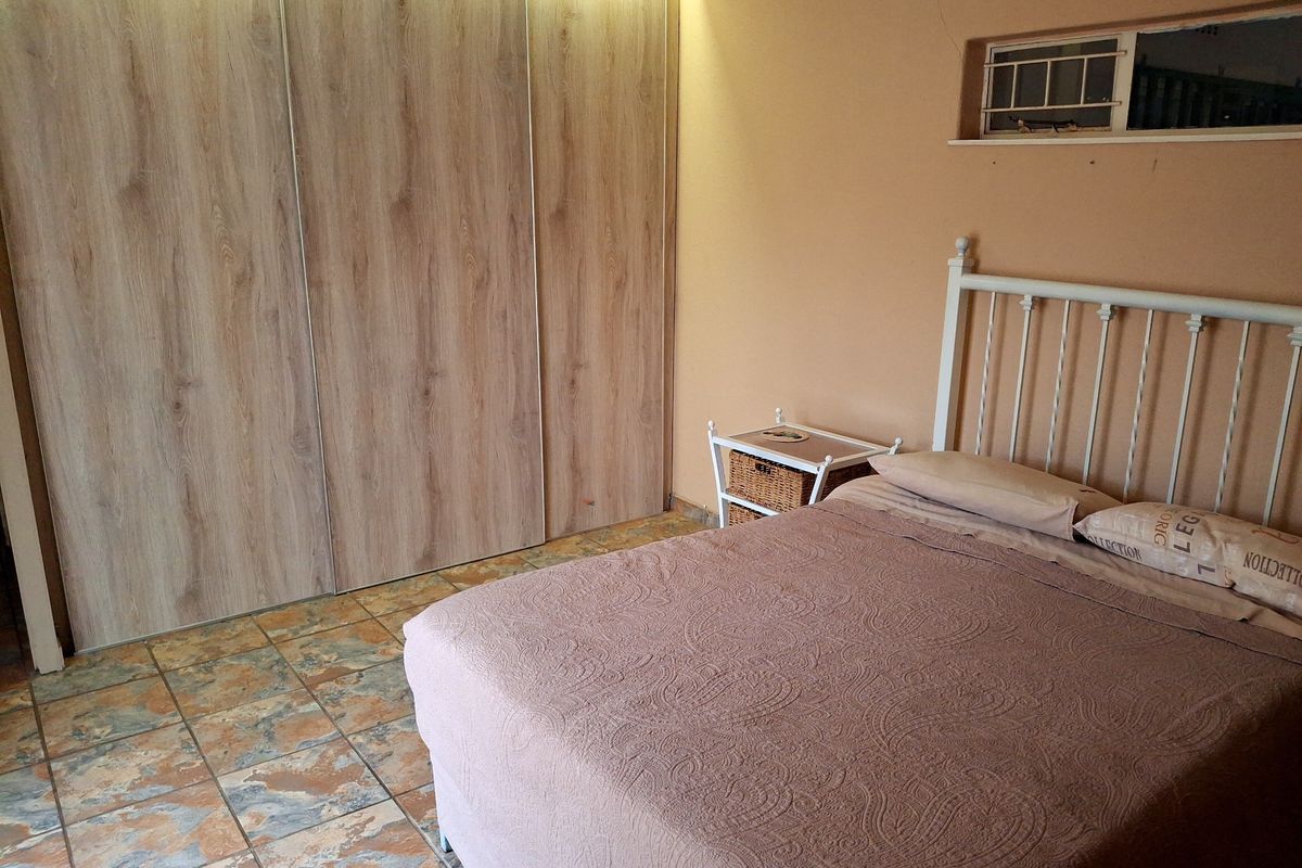 A bedroom featuring built-in wooden cupboards, tiled flooring, and a high-level window, offering a functional space with potential for cosmetic updates.