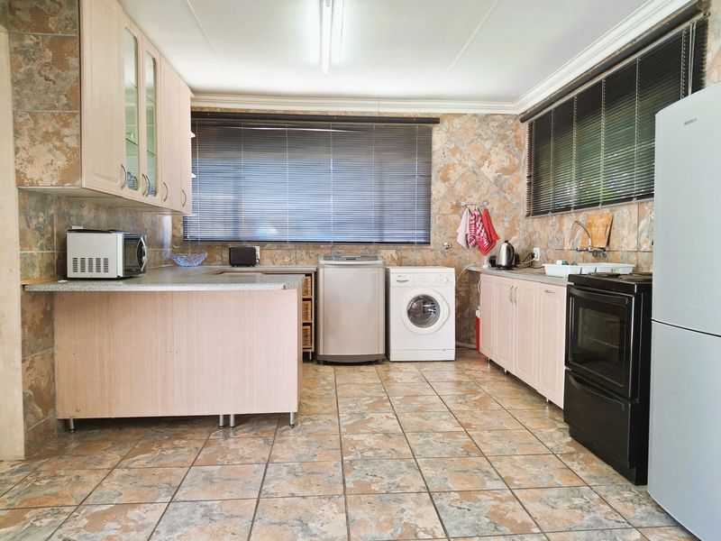 Functional kitchen featuring laminate cabinetry, stone-look wall and floor tiles, and integrated laundry appliance space with ample counter area.