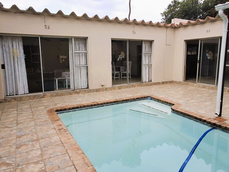 A paved courtyard area featuring a swimming pool with brick coping, surrounded by multiple sliding glass doors providing access to the interior living spaces.