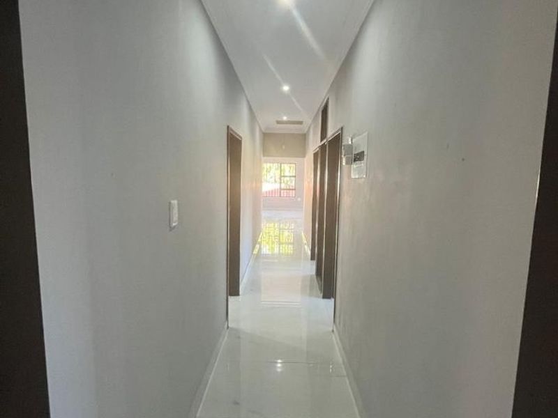 A clean, well-lit hallway featuring modern tiled flooring and recessed downlighting, providing access to multiple rooms within the home.