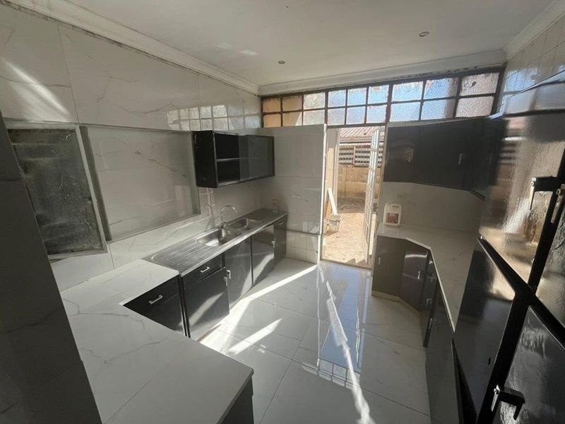 A functional kitchen featuring dark cabinetry, marble-look wall tiles, and tiled flooring, with direct access to the rear exterior area.
