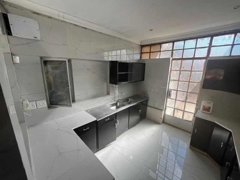 A functional kitchen featuring black cabinetry, marble-look tiled countertops, and a stainless steel double sink, with direct access to an outdoor area.