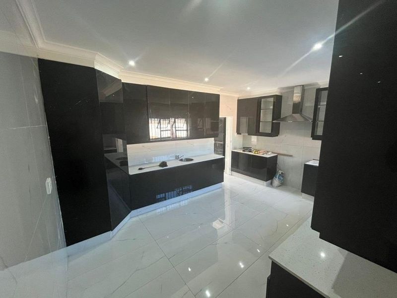 Modern kitchen featuring high-gloss black cabinetry, stone countertops, stainless steel extractor fan, and polished porcelain floor tiles in a clean, contemporary layout.