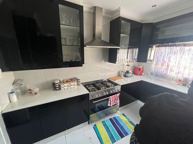 Modern kitchen featuring sleek black cabinetry, stone countertops, a gas stove with stainless steel extractor fan, and polished tiled flooring.