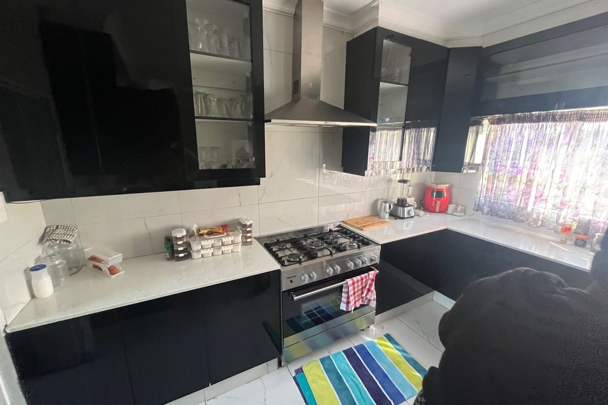 Modern kitchen featuring sleek black cabinetry, stone countertops, a gas stove with stainless steel extractor fan, and polished tiled flooring.