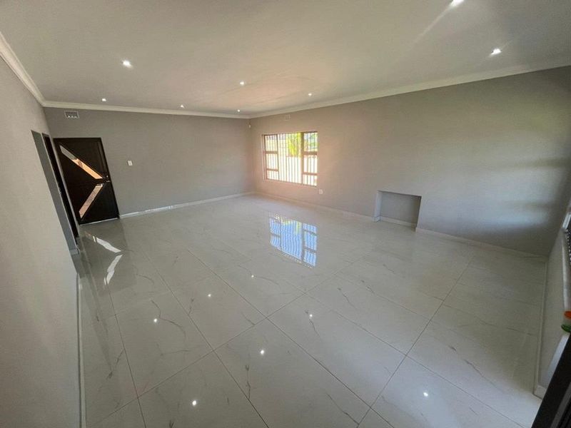 A spacious, empty living room featuring polished porcelain floor tiles, recessed downlights, and a neutral color palette, ready for personalization.
