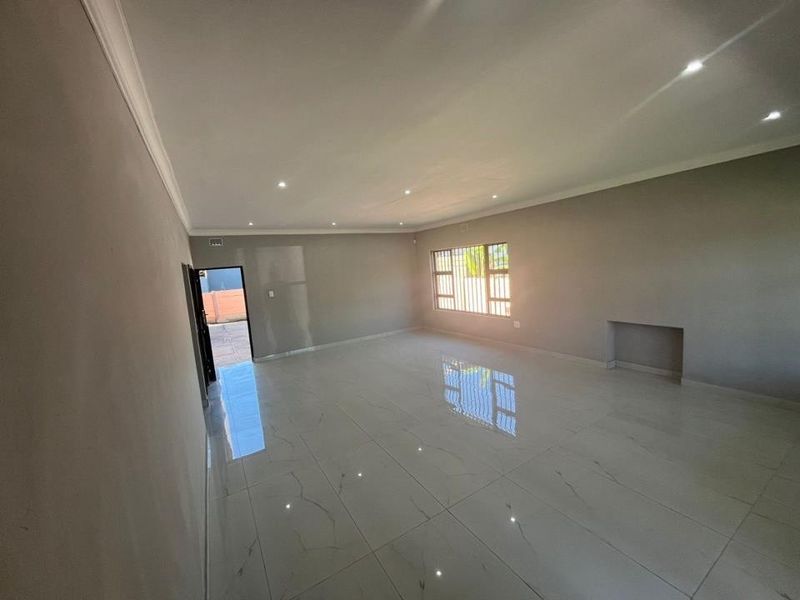A spacious, empty living area featuring modern porcelain floor tiles, recessed downlighting, and a built-in wall niche, offering a clean and neutral canvas.
