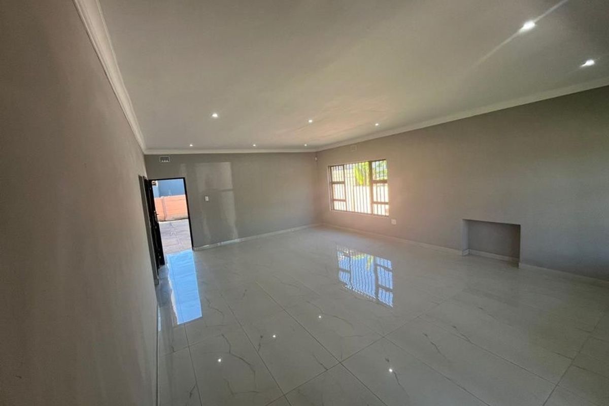 A spacious, empty living area featuring modern porcelain floor tiles, recessed downlighting, and a built-in wall niche, offering a clean and neutral canvas.