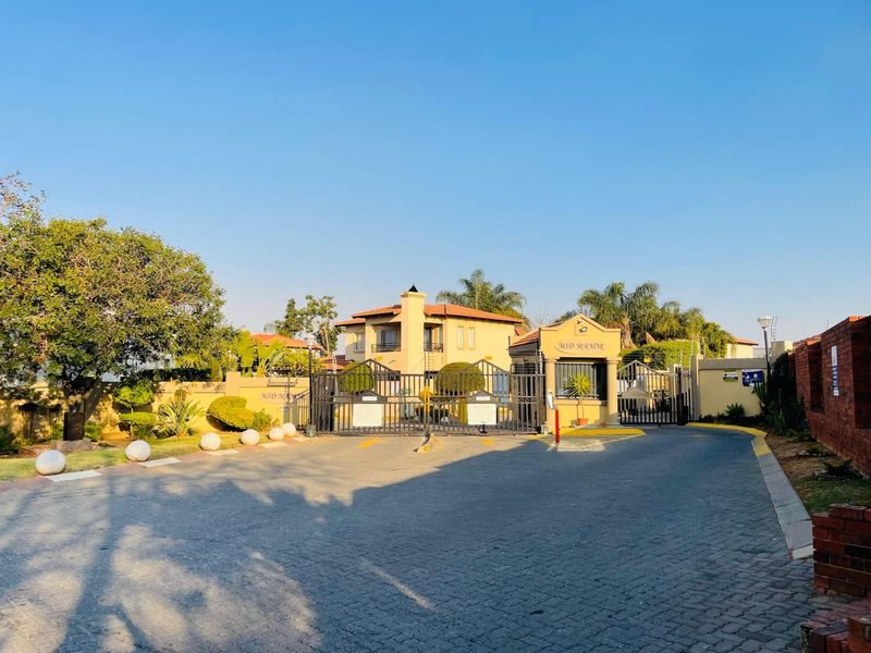 The entrance to Mid Manor estate featuring a secure gated access point, guard house, and paved driveway with perimeter walling.