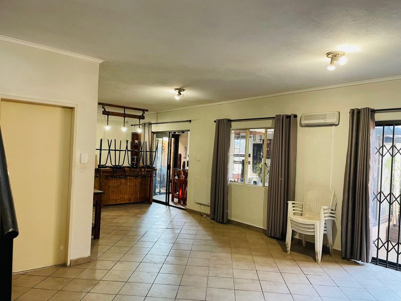 Spacious living area featuring tiled flooring, an air conditioning unit, and a built-in bar counter, with direct access to the outdoor area via sliding doors.