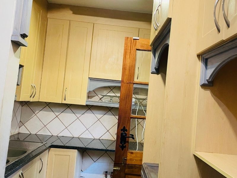 A compact scullery area featuring laminate cabinetry, granite countertops, and a tiled backsplash, currently requiring minor repairs and cosmetic updates.