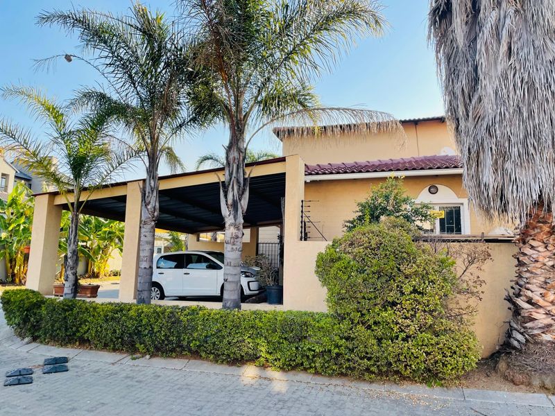 Front exterior view of the property featuring a covered carport, paved driveway, and established garden hedge with electric security fencing.