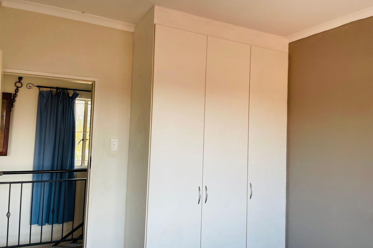 A bedroom interior featuring a large built-in wardrobe with white doors and a view through the doorway to an adjacent landing area.