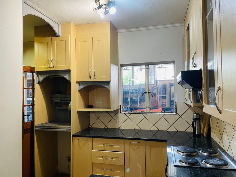 A functional kitchen featuring light wood cabinetry, dark granite countertops, a built-in electric hob, and a tiled backsplash with security-barred window.