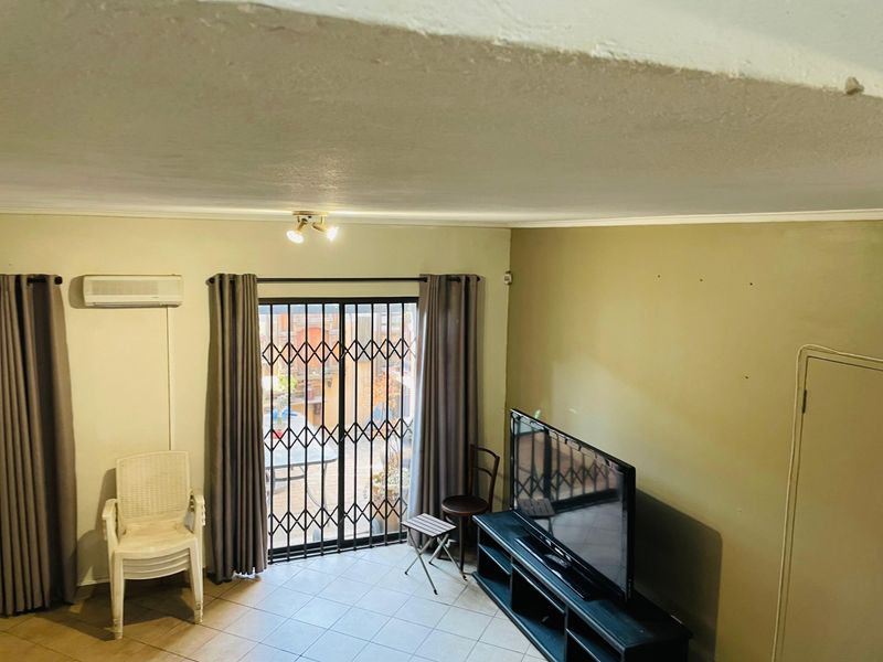 A living room featuring tiled flooring, an air conditioning unit, and a sliding glass door with a security gate leading to an outdoor area.