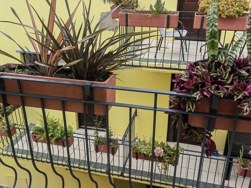A multi-level balcony area featuring wrought iron railings, tiled flooring, and yellow exterior walls with visible plaster damage.