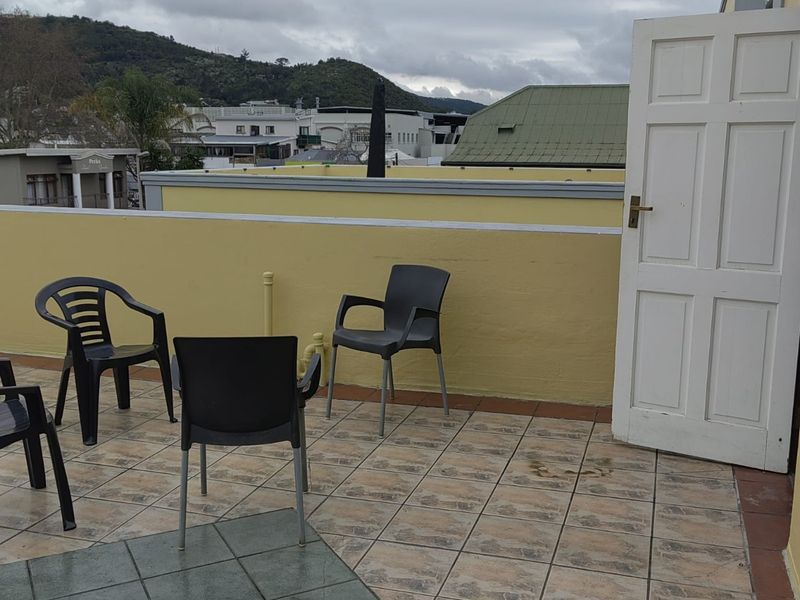 An open-air balcony featuring tiled flooring, a parapet wall, and an exterior door, offering elevated views of the surrounding neighborhood.