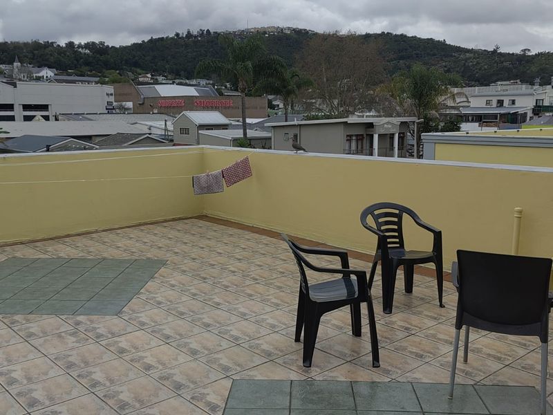An open-air rooftop balcony featuring tiled flooring and a surrounding parapet wall, offering expansive views of the surrounding neighborhood.