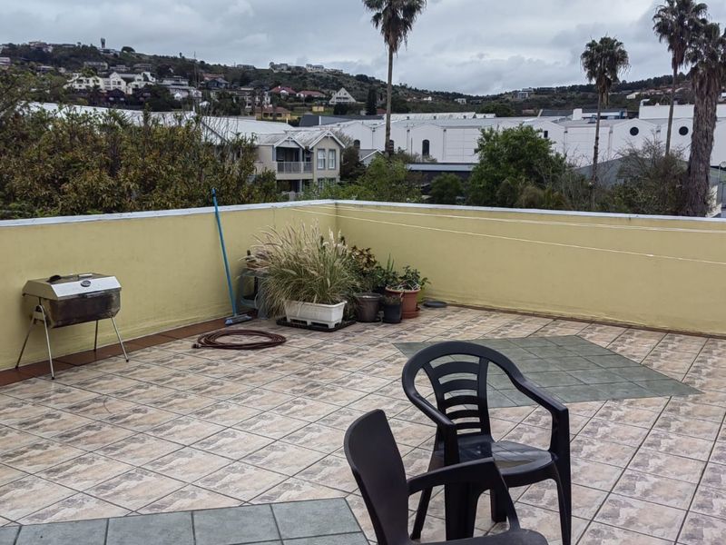 An open-air balcony featuring tiled flooring and a surrounding parapet wall, offering an elevated view of the surrounding neighborhood.