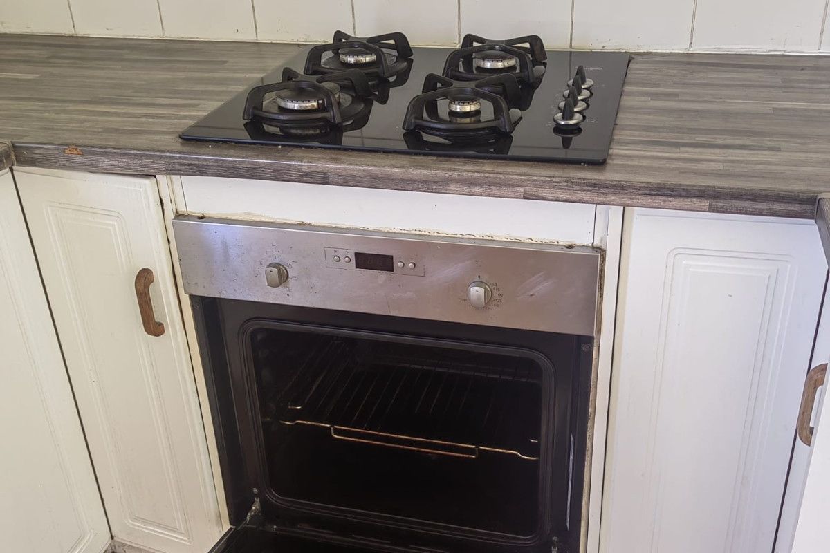 A kitchen area featuring a built-in gas hob and oven with laminate countertops and tiled backsplash, showing signs of wear and tear.