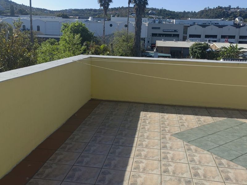 An open-air balcony featuring tiled flooring and a parapet wall, offering an elevated view of the surrounding neighbourhood.