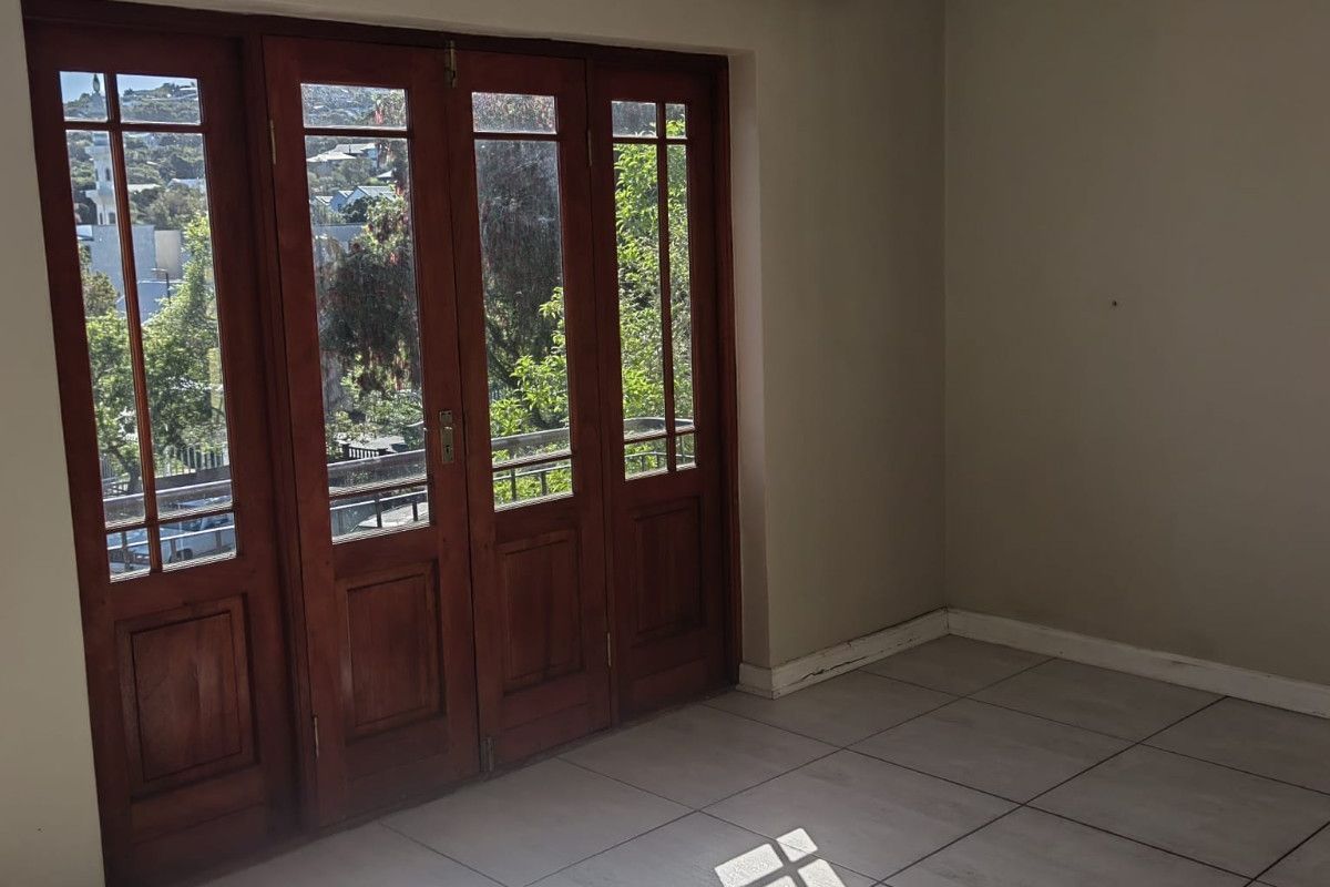 An empty living area featuring neutral tiled flooring and large wooden-framed glass folding doors that provide natural light and access to the outdoors.