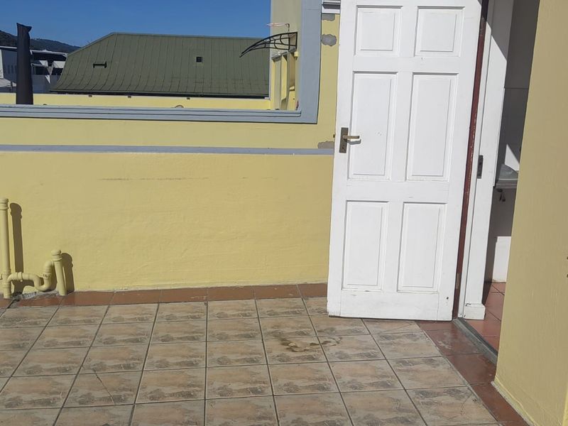 An open-air balcony area featuring tiled flooring and a parapet wall, providing direct access to the interior through a single door.
