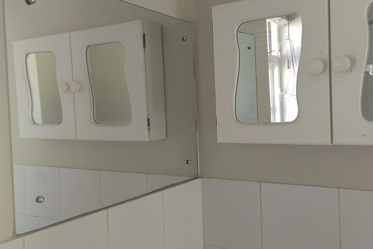 A bathroom vanity area featuring a wall-mounted medicine cabinet, a large mirror, and white ceramic wall tiling.
