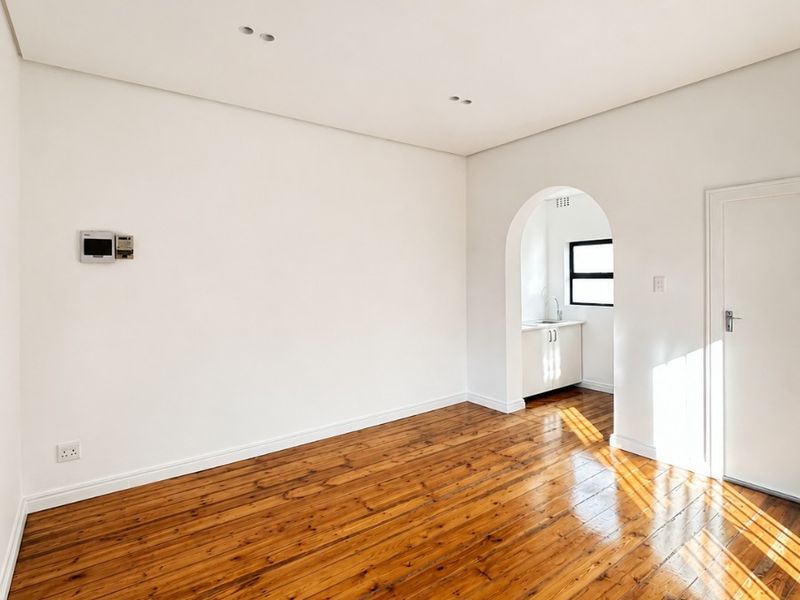 A bright, empty living room featuring polished hardwood floors, recessed lighting, and a charming arched doorway leading to an adjacent space.