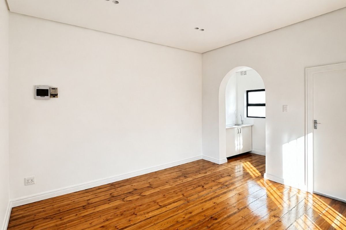 A bright, empty living room featuring polished hardwood floors, recessed lighting, and a charming arched doorway leading to an adjacent space.