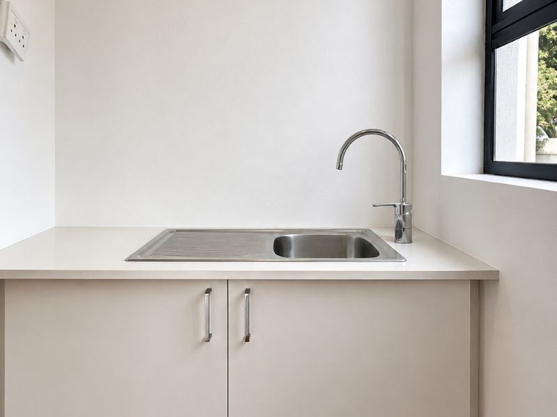 A clean and functional laundry area featuring a stainless steel sink, modern mixer tap, and built-in cabinetry with a stone countertop.
