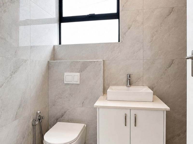 Modern bathroom featuring floor-to-ceiling stone-look tiling, a wall-mounted toilet, and a sleek vanity with a vessel sink.