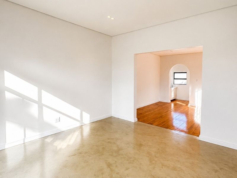Bright and spacious living area featuring polished concrete floors, recessed lighting, and an arched transition to an adjoining room with hardwood flooring.
