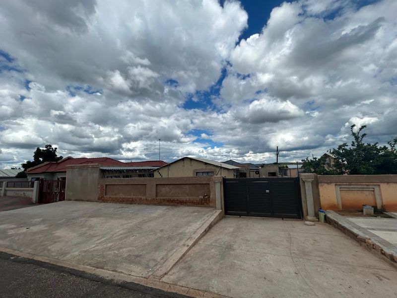 Front exterior view of the property featuring a concrete driveway, perimeter wall, and metal gate entrance.