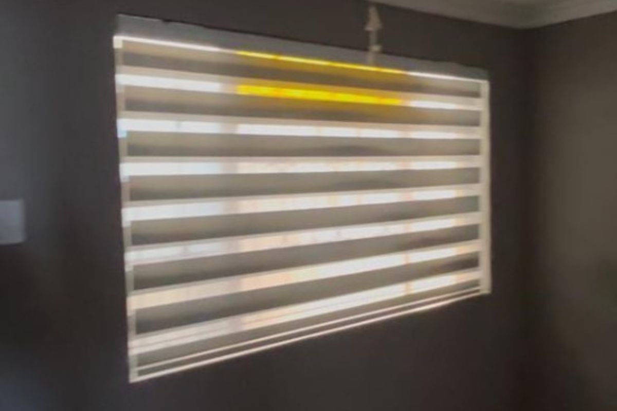 A simple bedroom interior featuring tiled flooring and modern zebra blinds on the window.
