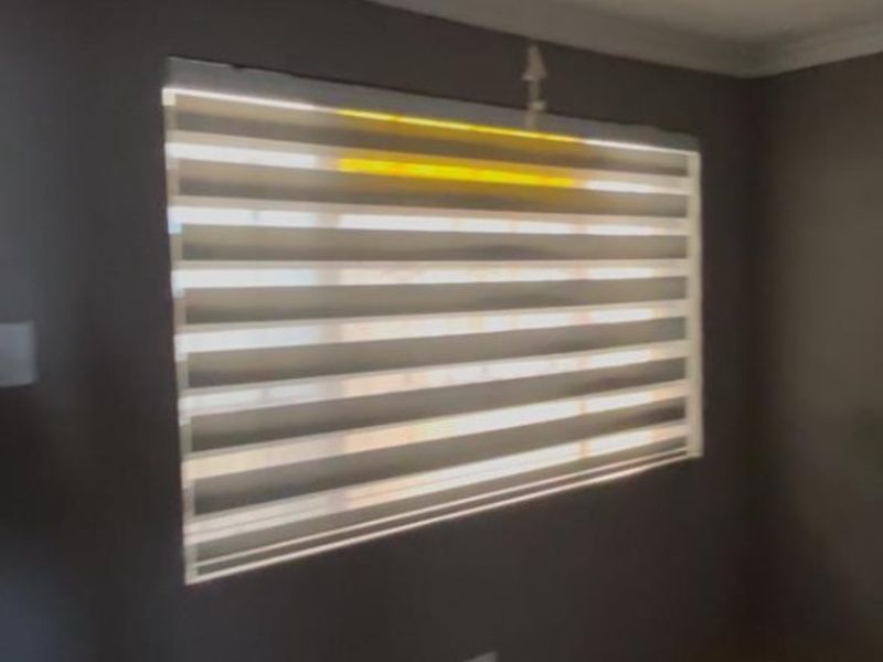 A simple bedroom interior featuring tiled flooring and modern zebra blinds on the window.